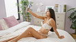 © Krakenimages.com - Sensual morning, young indian woman confidently taking a sexy selfie on her smartphone while sitting in bed, looking through the lens with a playful smile in her cozy bedroom