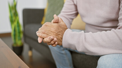 Wall Mural - A senior man clasps his hands in a cozy living room, portraying contemplation and tranquility indoors.