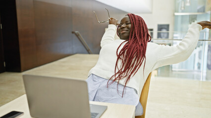 Sticker - African american woman with braids stretching joyfully in a modern indoor office setting