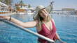 © Krakenimages.com - A smiling woman in a hat enjoys the luxury pool in daylight, exuding carefree summer vibes.
