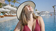 © Krakenimages.com - Smiling woman in sunhat enjoys luxury poolside ambiance, embodying leisure and elegance.