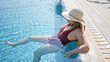 © Krakenimages.com - A young adult woman in a swimsuit and sunhat lounges by a poolside on a sunny summer day, conveying leisure.