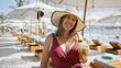 © Krakenimages.com - A smiling woman in a hat and swimsuit holds a mojito at a luxurious poolside beach club.