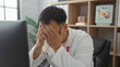 © Krakenimages.com - Handsome young chinese male doctor in a clinic room looking stressed, covering his face with his hands, epitomizing burnout in a medical workplace.