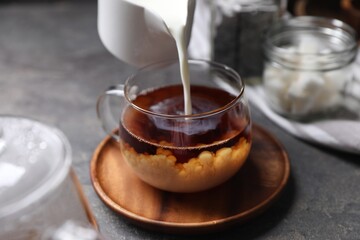 Sticker - Pouring milk into cup of tea on grey table, closeup