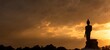 © BESTIMAGE - Stand big Buddha Statue in silhouette sun set Light background in park of Thailand temple.Yellow orange light silhouette dark shadow of image Buddha statue stand Buddha tall walk in sun light cloud.