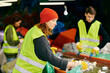 © LIGHTFIELD STUDIOS - A young woman in a green vest and a man in a black shirt, wearing gloves, sorting trash as eco-conscious volunteers.