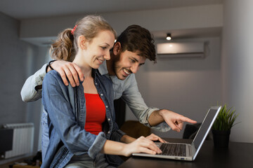 A joyful young couple collaborates using a laptop in a well-lit modern home setting, sharing a positive, productive moment.