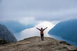 © Fokke Baarssen - A lone hiker stands with arms outstretched on the edge of the famous Preikestolen cliff in Norway, overlooking a stunning fjord and the surrounding mountains. Preikestolen, Norway