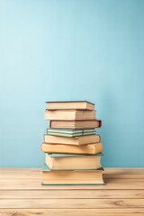 Wall Mural - Tall stack of various hardcover books positioned on a wood surface against a serene blue backdrop with ample space for text