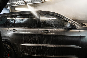 Wall Mural - Washing off the foam with high-pressure water. Manual washing of car with water at a self-service car wash.