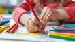 © K-MookPan - Close-Up Macro: A close-up of a child's hands holding a crayon and drawing on a piece of paper, with other art supplies scattered around