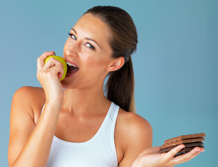 Wall Mural - Portrait, woman and eating apple with chocolate isolated on studio with smile, happy and diet in blue background. Smile, green fruit and young vegetarian person for detox, vegan or health decision