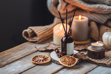 Hello autumn, cozy slow living. Pumpkin, aromatic candle, warm sweaters, dry fall leaves, cinnamon, anise in golden lights with bokeh on white wooden background. Thanksgiving apartment decor