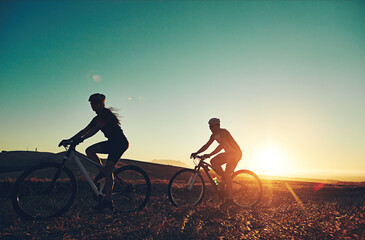 Sunset, silhouette and people on bicycle with fitness, race and exercise in nature together. Cycling, adventure and friends with mountain bike in evening for outdoor workout, blue sky and grass path