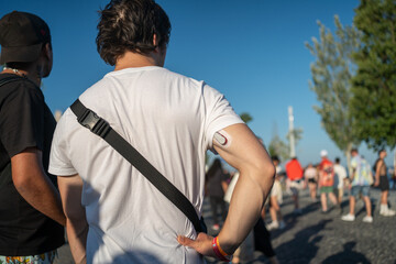 rear view of anonymous male tourist with glucose monitoring system sensor on back of arm, standing o