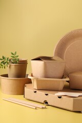 Sticker - Eco friendly food packaging. Paper containers, tableware and green twigs on pale yellow background