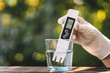 © diy13 - Water quality meter tester submerged in drinking glass, on blurred background of nature. Measuring harmful impurities, purifying water for healthy eating. distilled water