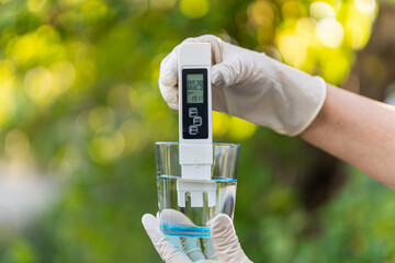 pH meter in hands with gloves, glass of water on blurred background of nature. Measurement of characteristics of drinking water. hardness of water. pure distilled water. high values salt impurities