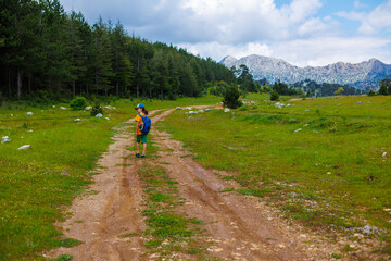 Sticker - Traveling child. a tourist with a backpack walks along a mountain road. hiking and active healthy lifestyle.