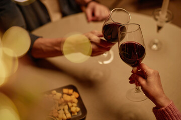 High angle closeup of adult couple toasting with wine glasses over table enjoying romantic dinner date with bokeh effect copy space