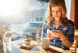 © ReadyAtTheEase/peopleimages.com - Woman, coffee and smartphone in cafe for breakfast, app and digital menu with happiness in city. Girl, smile and muffin in Sweden at restaurant with phone for email, chat and online customer feedback