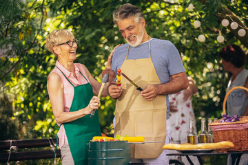 Elderly couple celebrate the 4th of July in their backyard. They are making barbeque, vegetables, and drinking beverages while enjoying and making memories