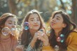 © DK_2020 - Three happy women have fun playing a game of blowing bubbles in a park. Caucasian friends enjoy hanging out together outdoors celebrating their friendship