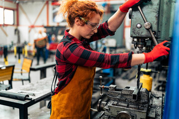 A young woman in STEM adjusts a machine with a drill before starting work on a new project, uses protective equipment and practices safe work