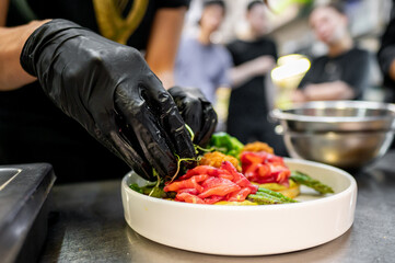 Sticker - Close-up of hands in black gloves garnishing a fresh salad with red salmon and green vegetables in a professional kitchen