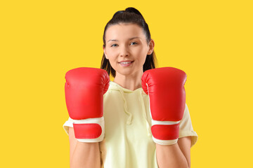 Poster - Sporty young woman in boxing gloves on yellow background