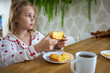 © evgeniia_1010 - A cute blonde girl in beautiful pajamas is sitting at a cozy table in the kitchen and having a delicious and healthy breakfast. The concept of proper and balanced nutrition.