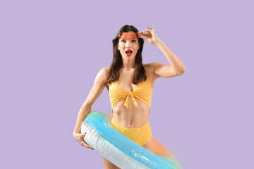 Poster - Surprised young woman in beachwear with swim ring on lilac background