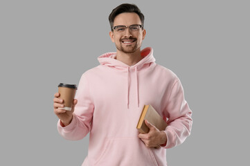 Wall Mural - Young man in eyeglasses holding book and coffee to-go on grey background