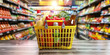 © Planetz - Shopping cart filled with a variety of fresh groceries in a supermarket aisle. The cart contains fruits, vegetables, meats, canned goods,
