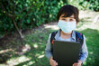 © peopleimages.com - Boy, face mask and student with book outdoor, confident and backpack for education. Male person, learner and safety for virus or protect against germs, learning and child development at academy