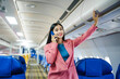 © Phushutter - A young Asian female airplane passenger sits by the window during the flight, holding her boarding pass, with her carry-on luggage stored overhead, wearing her seatbelt, and enjoying the journey.