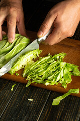 Wall Mural - Cutting cabbage for a vegetarian dish. Knife in the hand of a cook for shredding fresh cabbage on a kitchen board.