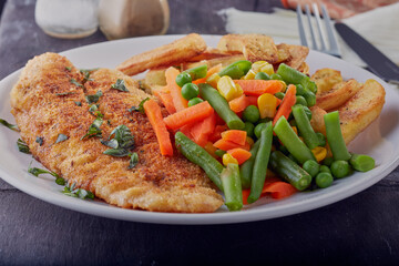 Bread crumbed fish fillet with chips and vegetables.