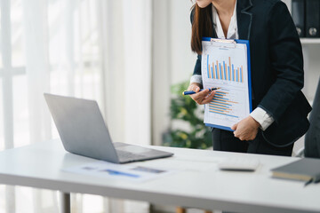 Wall Mural - Businesswoman in a business suit is standing at a desk with a laptop and a clipboard