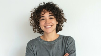 Wall Mural - Smiling woman with curly hair, arms confidently crossed, simple white background, casual look, isolated, cheerful and confident, copy space