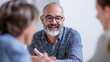 © Nataliia_Trushchenko - A man with glasses is smiling and talking to two other people. Scene is friendly and positive. a professor facilitating a group discussion,
