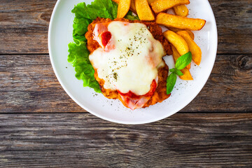 Wall Mural - Milanesa Napolitana - fried breaded cutlet with ham, mozzarella cheese and tomato sauce on wooden background
