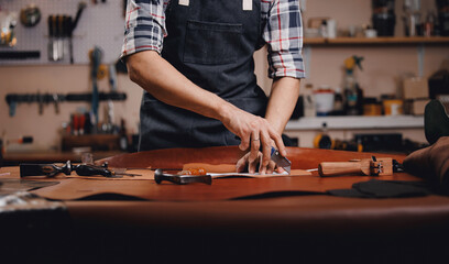 Cobbler Man tailor chooses roll of brown leather for sewing a bag or shoes made of skin in workshop. Banner of industry leather products