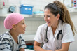 © SnapVault - A young cancer patient wearing a pink headscarf smiles at a supportive nurse in a hospital setting. The nurse, dressed in a white uniform, shares a moment of joy, care and positivity