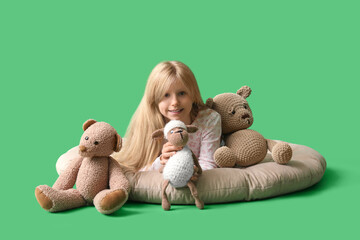 Wall Mural - Cute little girl with plush toys lying on green background