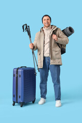 Sticker - Male tourist in warm clothes with trekking poles, backpack and suitcase on blue background