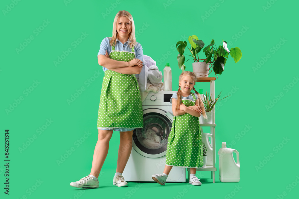 Happy mother and her little daughter doing laundry on green background