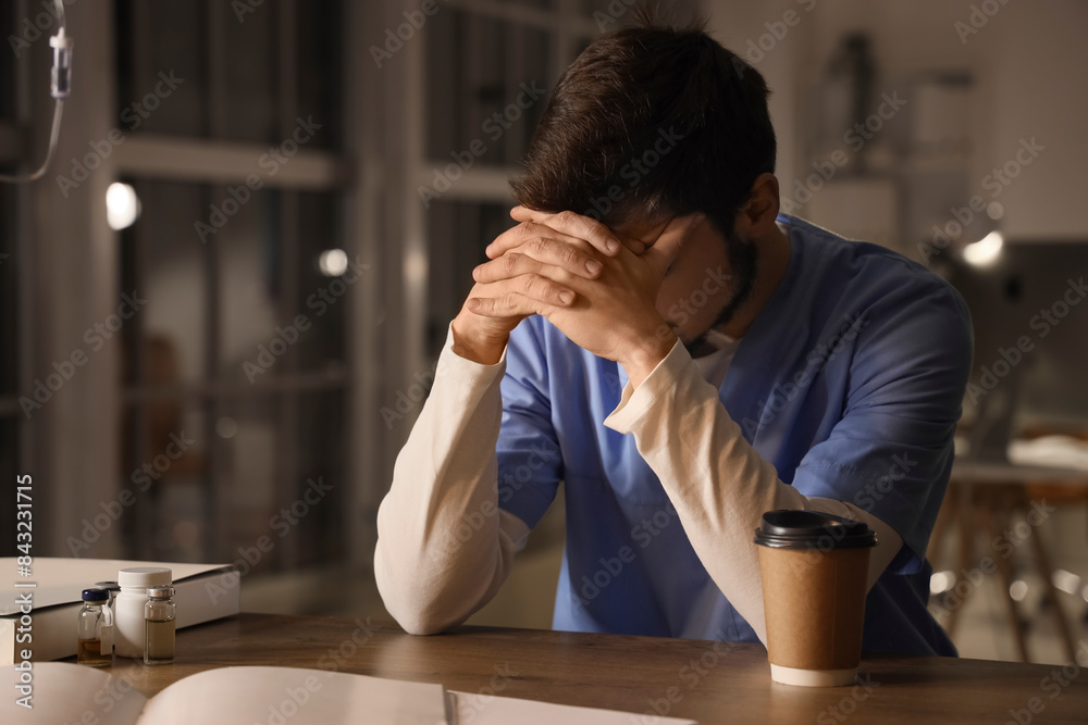 Tired male nurse working evening shift at desk in clinic