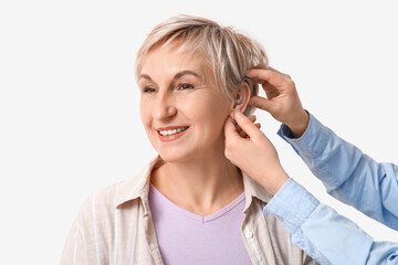 Poster - Young woman putting hearing aid in mature woman's ear on white background